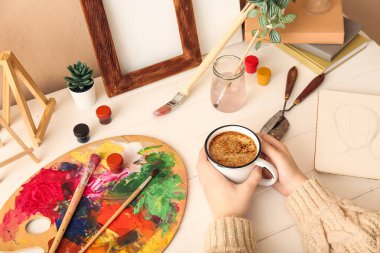 Beyaz ahşap masada bir fincan kahveli kadın sanatçı, yakın plan.