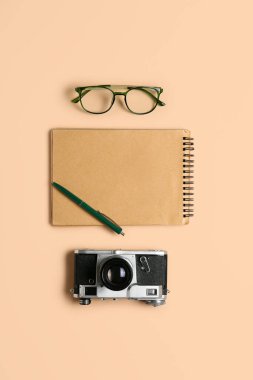 Bej arka planda kalem, fotoğraf makinesi ve gözlüklü defter.