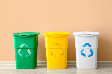 Bej duvarın yanında geri dönüşüm sembolü olan farklı çöp bidonları
