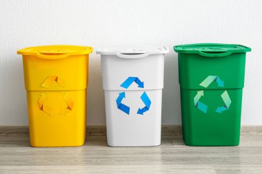 Beyaz duvarın yanında geri dönüşüm sembolü olan farklı çöp bidonları