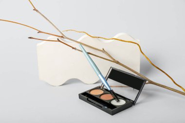 Göz falı paleti, kirpik fırçası, ağaç dalı ve gri arka planda sıva kürsüsü