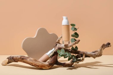 Alçı podyumlu kompozisyon, makyaj vakfı şişesi, okaliptüs ve bej arka planda ağaç dalları