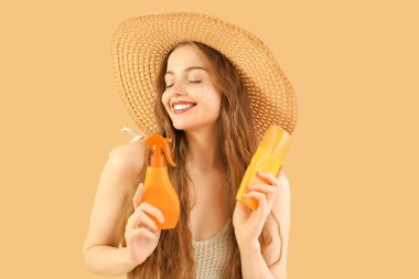 Bej arka planda güneş kremleri olan güzel genç bir kadın.