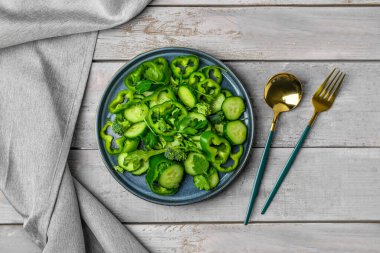 Gri ahşap arka planda yeşil sebzeli bir tabak salata.