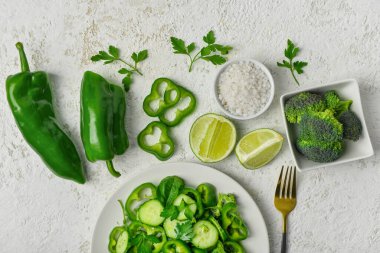 Yeşil sebzeli bir tabak salata ve arkaplanda malzemeler.