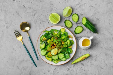 Yeşil sebzeli bir tabak salata ve gri grunge arka planda malzemeler.