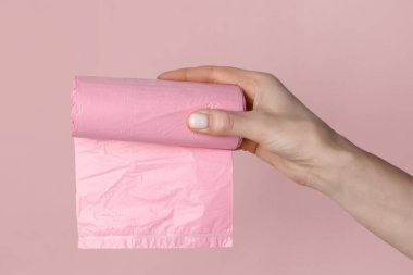 Pembe arka planda çöp torbası rulosu tutan kadın.