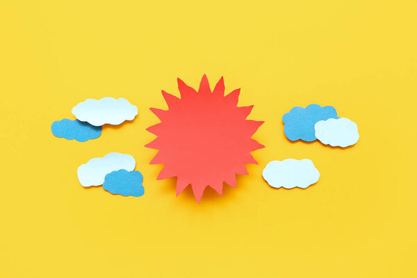 Composition with paper sun and clouds on yellow background