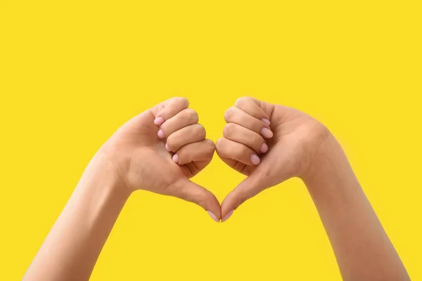 Woman making heart with her hands on yellow background