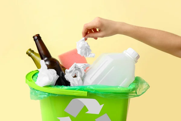 Woman throwing garbage into trash bin on yellow background, closeup