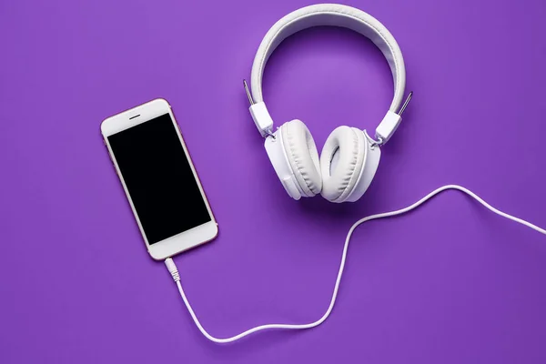 Mobile phone with headphones on purple background