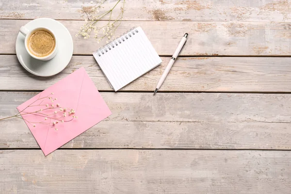 Kompozisyon defteri, zarf ve bir fincan kahve yıpranmış ahşap masada.