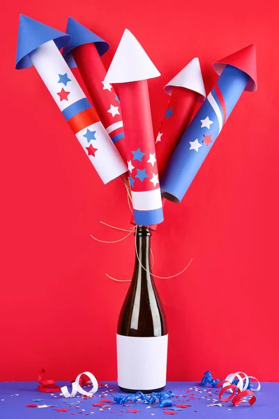 Bottle of champagne with firework rockets for Independence Day on red background