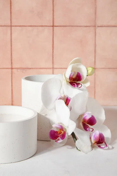 stock image Decorative plaster podiums and beautiful orchid flowers on white table near tiled wall