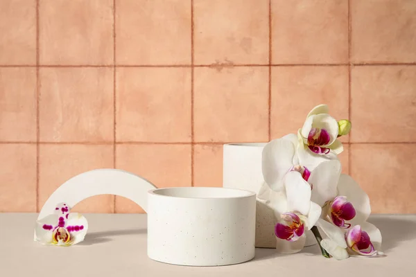 Stock image Decorative plaster podiums and beautiful orchid flowers on white table near tiled wall