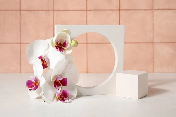 stock image Decorative plaster podiums and beautiful orchid flowers on white table near tiled wall