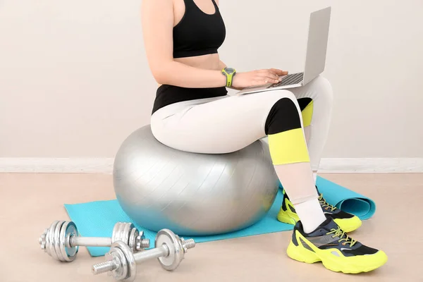 Sporty woman using laptop on fitball in gym