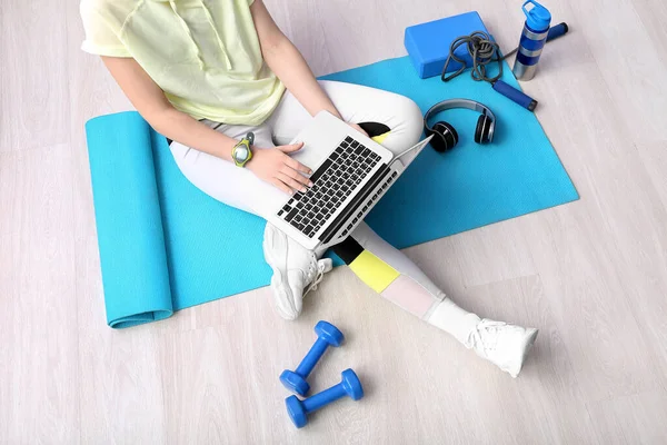 Sporty woman using laptop on mat in gym