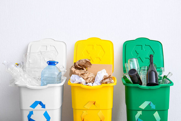 Trash bins with recycling symbol and different garbage near white wall