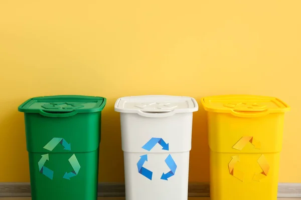 Different garbage bins with recycling symbol near yellow wall