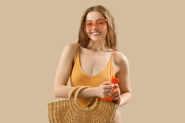 Schöne Junge Frau Mit Sonnencreme Und Strandtasche Auf Beigem Hintergrund — Stockfoto