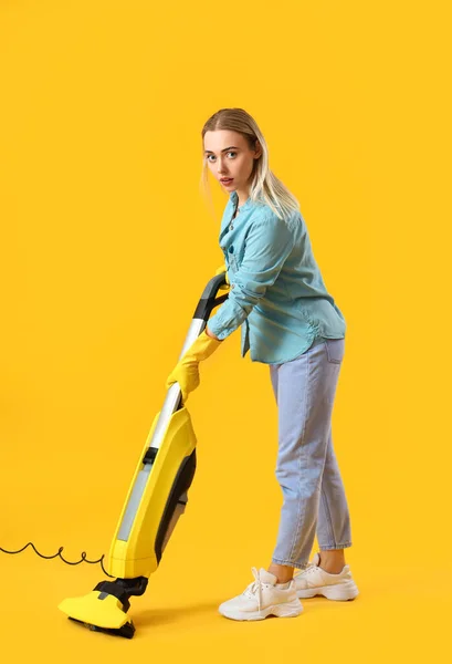 Young woman with vacuum cleaner on yellow background
