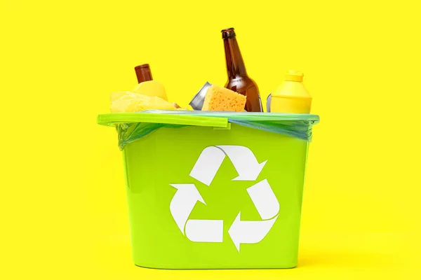 Trash bin with different garbage on yellow background