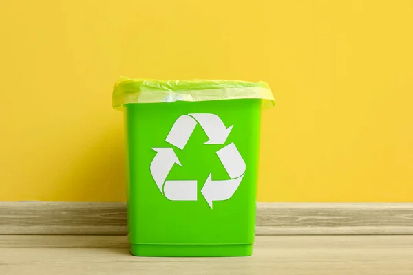 Trash bin with recycling symbol near yellow wall