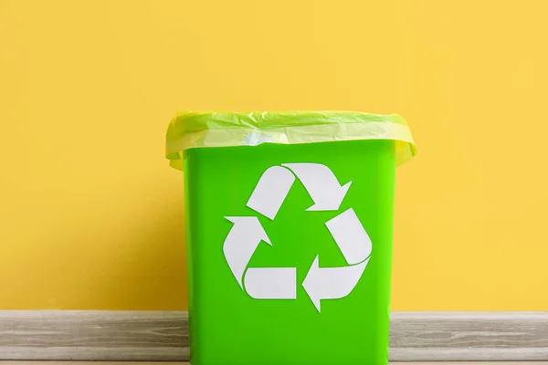 Trash bin with recycling symbol near yellow wall