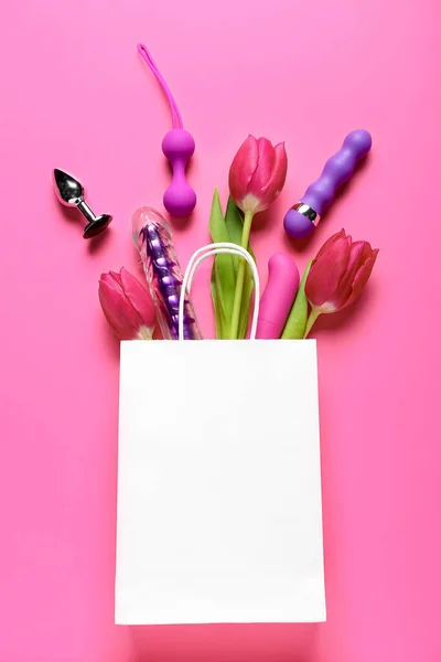 Paper bag with sex toys and tulips on pink background