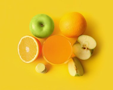 Bir bardak C vitamini tableti suda çözünmüş ve meyveler sarı arka planda.