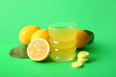 Bir bardak C vitamini tableti suda çözünmüş ve limonlar yeşil arka planda.
