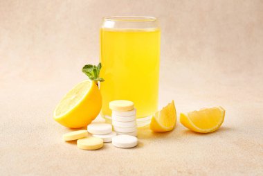 Bir bardak C vitamini tableti suda çözünmüş limonlar da bej grunge masasında.
