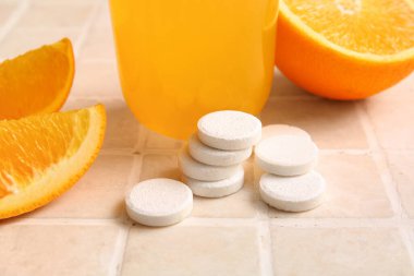 C vitamini tabletleri ve portakal tabletleri fayanslı masada.