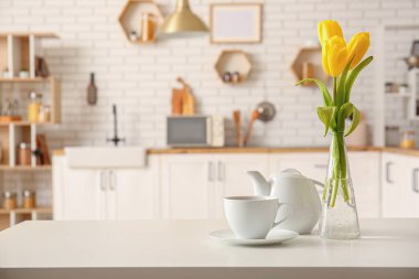 Çay fincanı, çaydanlık ve vazo. Modern mutfağın içindeki masada güzel lale çiçekleri var.