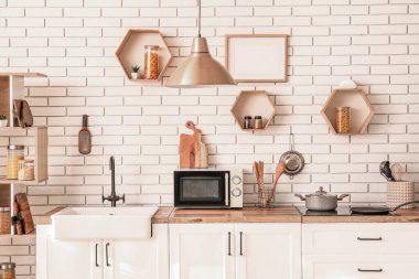 Modern mutfağın içinde lavabo, mikrodalga fırın ve beyaz tezgahlarda tencere var.