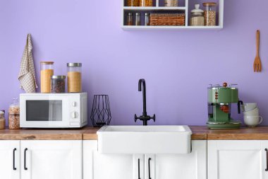 Lavabo, mikrodalga fırın ve eflatun duvarın yanında kahve makinesi olan mutfak tezgahları.