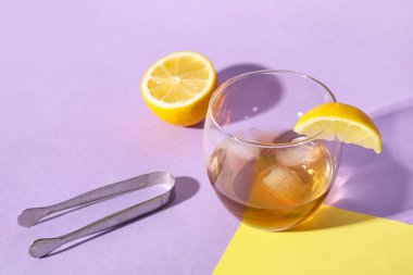 Bir bardak buzlu rom, limon dilimi ve renkli arka planda maşa.