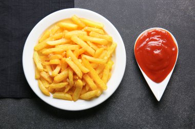 Koyu arkaplanda lezzetli patates kızartması ve ketçap tabağı.