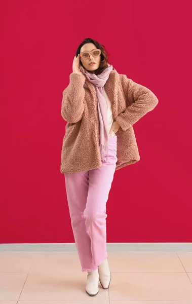 粉红墙壁附近穿着泰迪熊外套和太阳镜的时髦年轻女子 — 图库照片