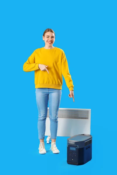 Young woman with portable gasoline generator and radiator on blue background