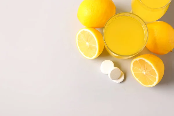 Glass of vitamin C effervescent tablet dissolved in water and lemons on grey background