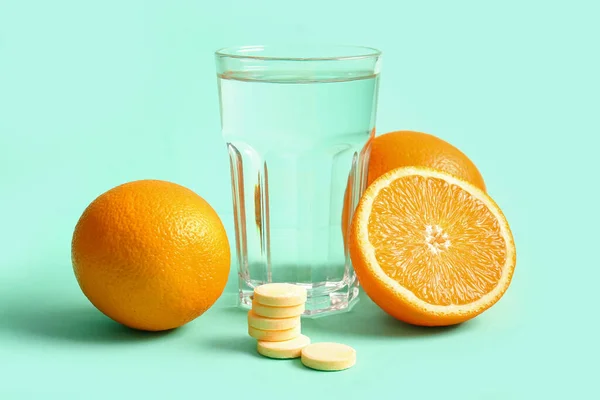 Glass of water, vitamin C effervescent tablets and oranges on turquoise background