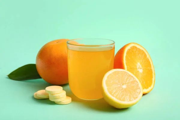Glass of vitamin C effervescent tablet dissolved in water and fruits on turquoise background