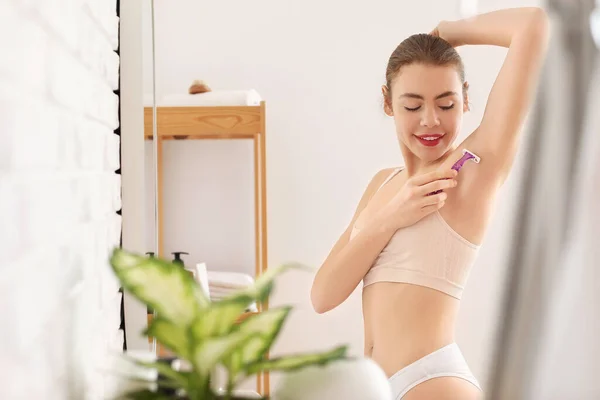 Young woman shaving her armpit with razor in bathroom