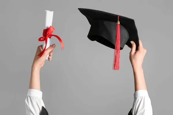 グレーを背景に卒業帽子と卒業証書を持つ女性 — ストック写真