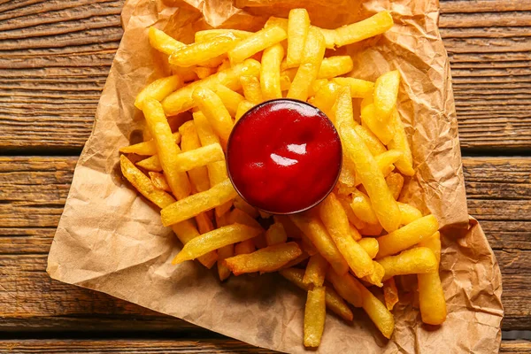 Baking paper with tasty french fries and ketchup on wooden background, closeup