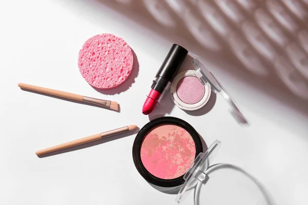 Lipstick, blush, eyeshadows, makeup brushes and sponge on light background