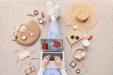 Bilgisayarlı ve aksesuarlı bir kadın bej halıdan alışveriş yapıyor.