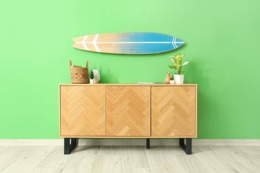 Odadaki yeşil duvarda asılı sandık dolusu çiçek ve sörf tahtası.